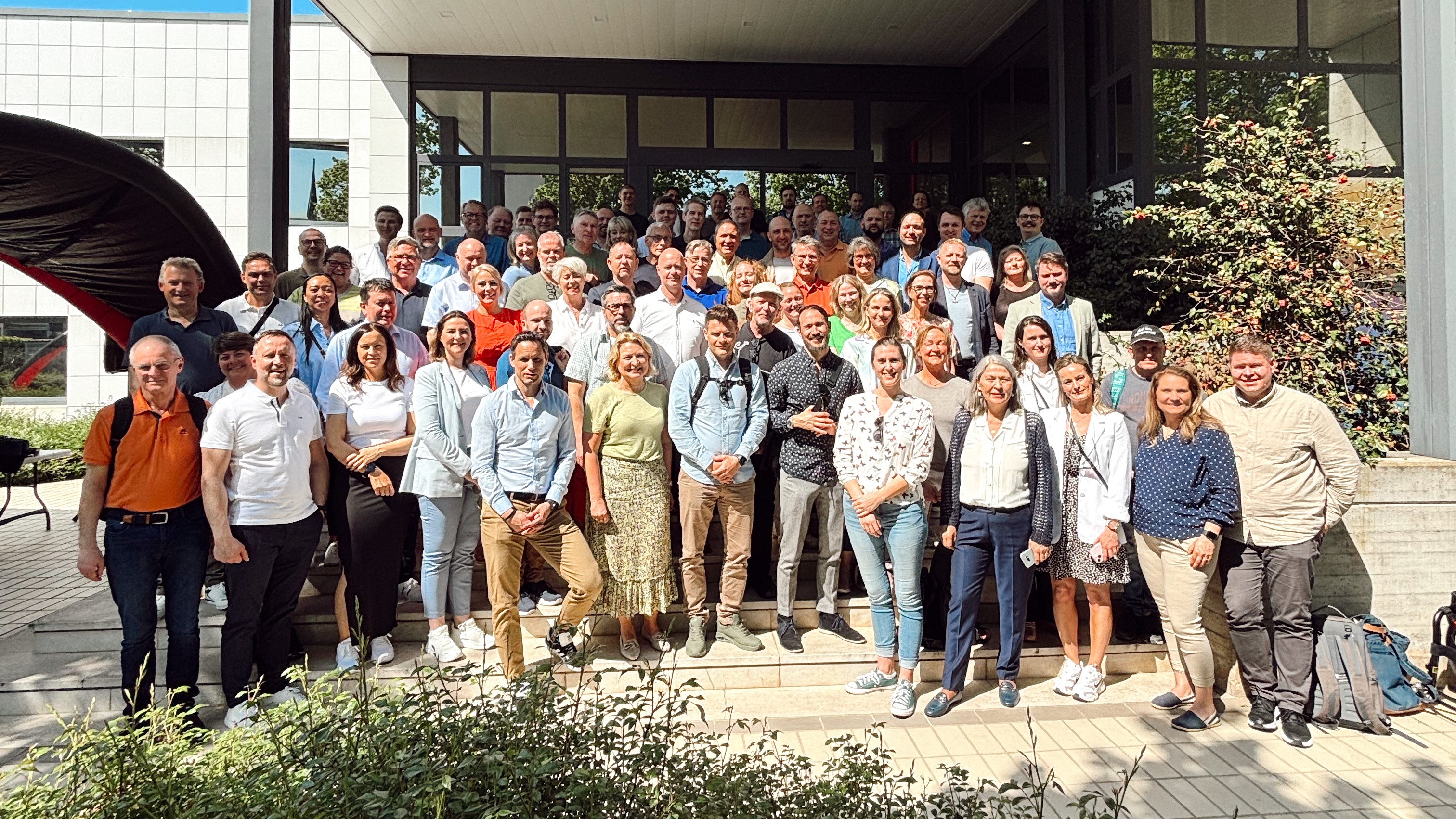 Stor gruppe med smilende culina-kollegaer samlet utenfor kontorbygning på en solrik dag